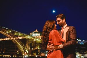 lovers posing at sunset with the lights of the city behind